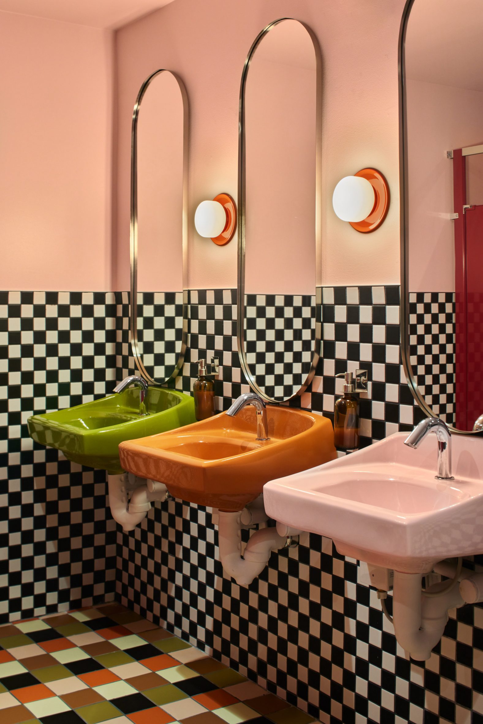 Bathroom with checkerboard tiles, coloured sinks and pill-shaped mirrors
