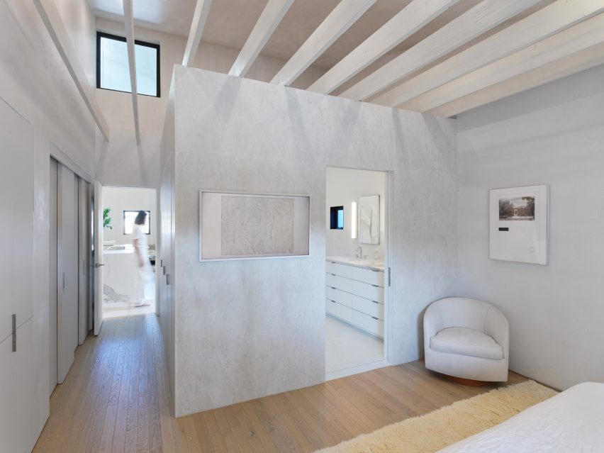 Белая спальня с деревянным полом и белыми перегородками, скрывающими ванную комнату.
