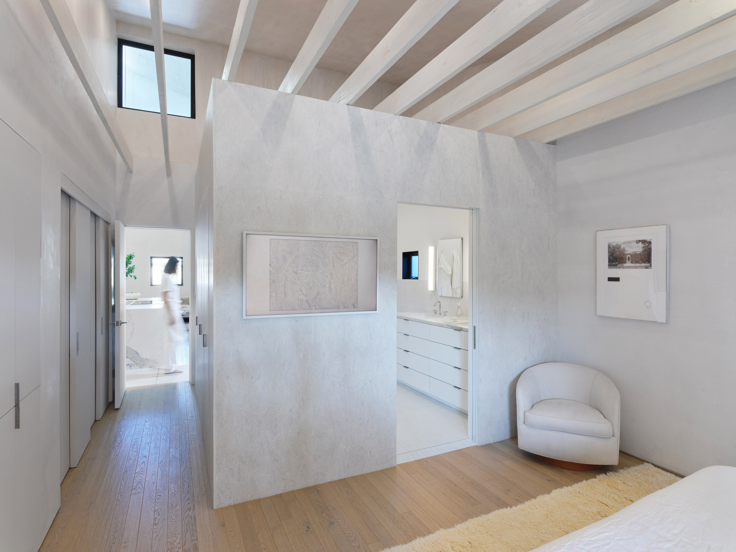 White bedroom with wooden floors and white partition walls concealing a bathroom