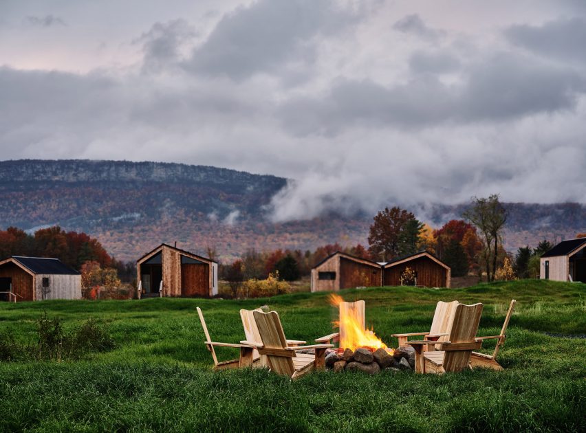Chairs surrounding a fire pit with cabins and mountain ridge in the distance