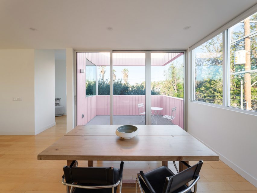 Столовая с деревянными полами и раздвижными стеклянными дверями, ведущими на террасу с розовыми стенами.