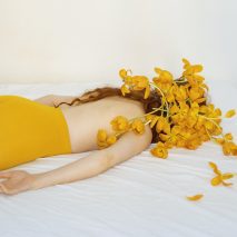 Photo of person in tights lying on a bed covered in yellow flowers by Iosonopipo