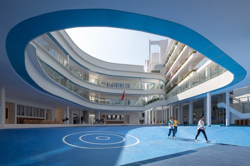 Curving classrooms surrounding a blue playground at Kindergarten of Museum Forest by Atelier Apeiron