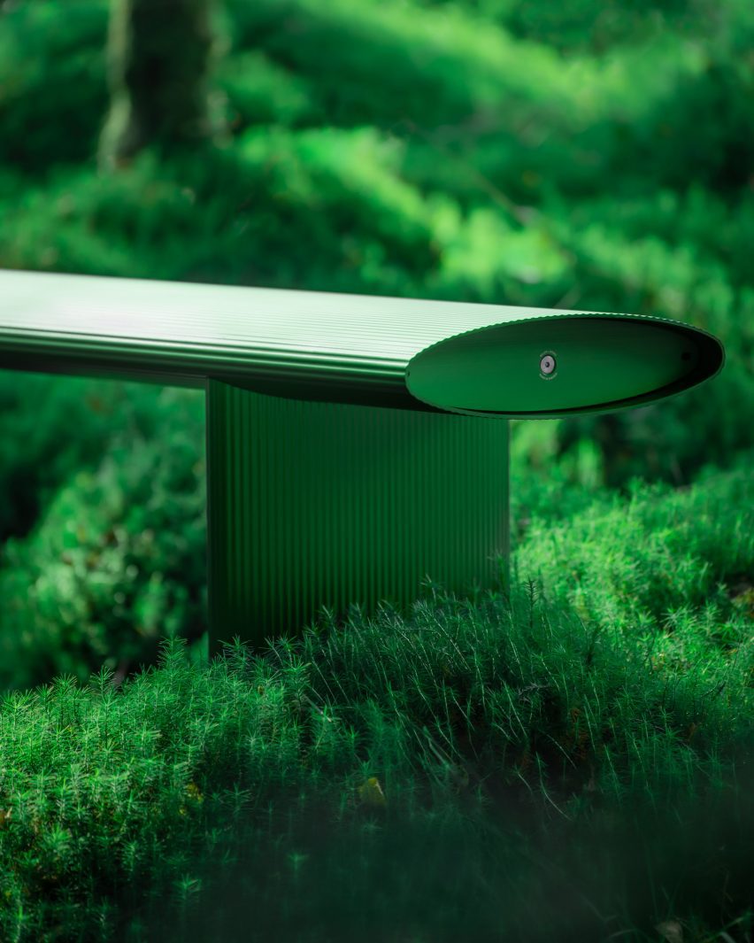 Photo of a green extruded metal bench sitting within a forest of dence foliage