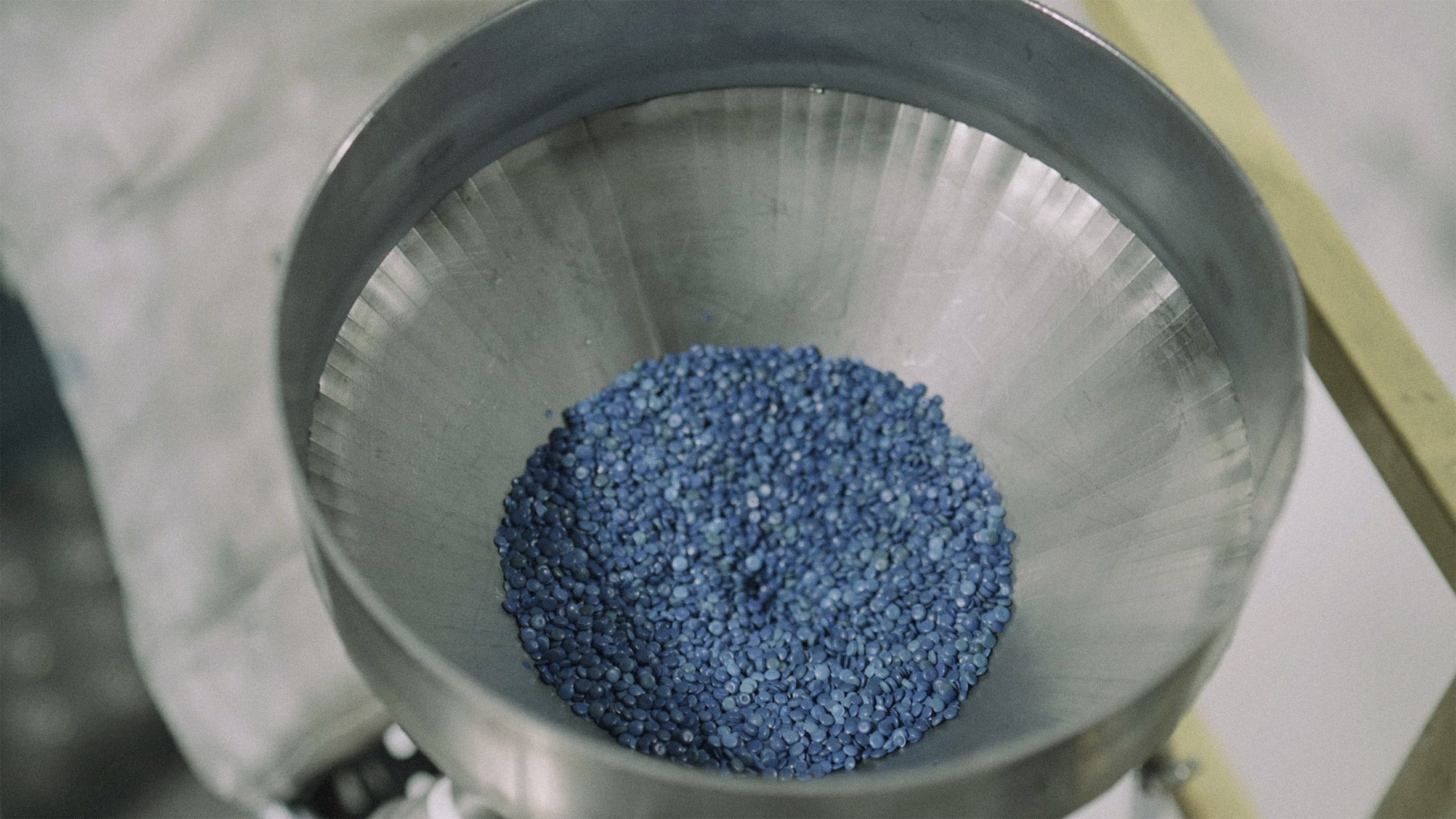 Photo of small, lentil-like blue pellets in a silver funnel