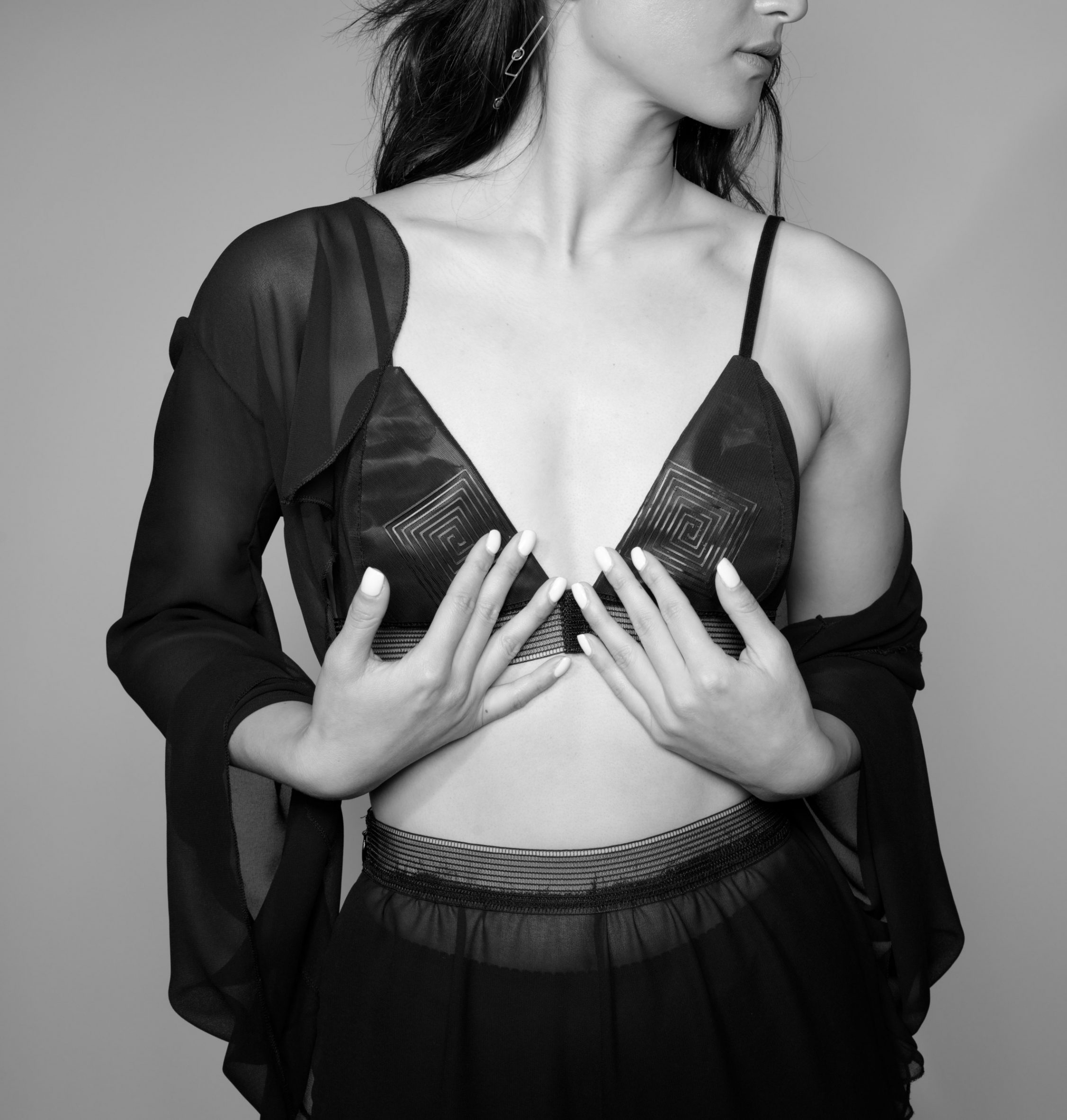 Black and white photo of a woman from the chin down wearing the black Enigma bralette and pants, with a light robe over the top