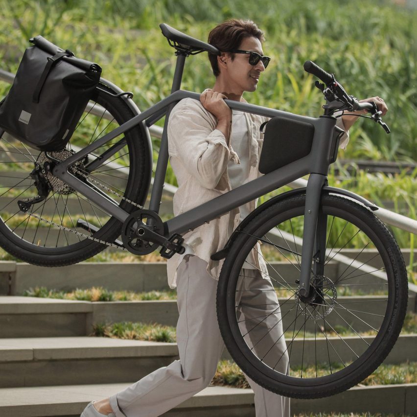 Photo of a youthful man in sunglasses carrying a Lemmo One bike on one shoulder as he walks down a set of steps outdoors