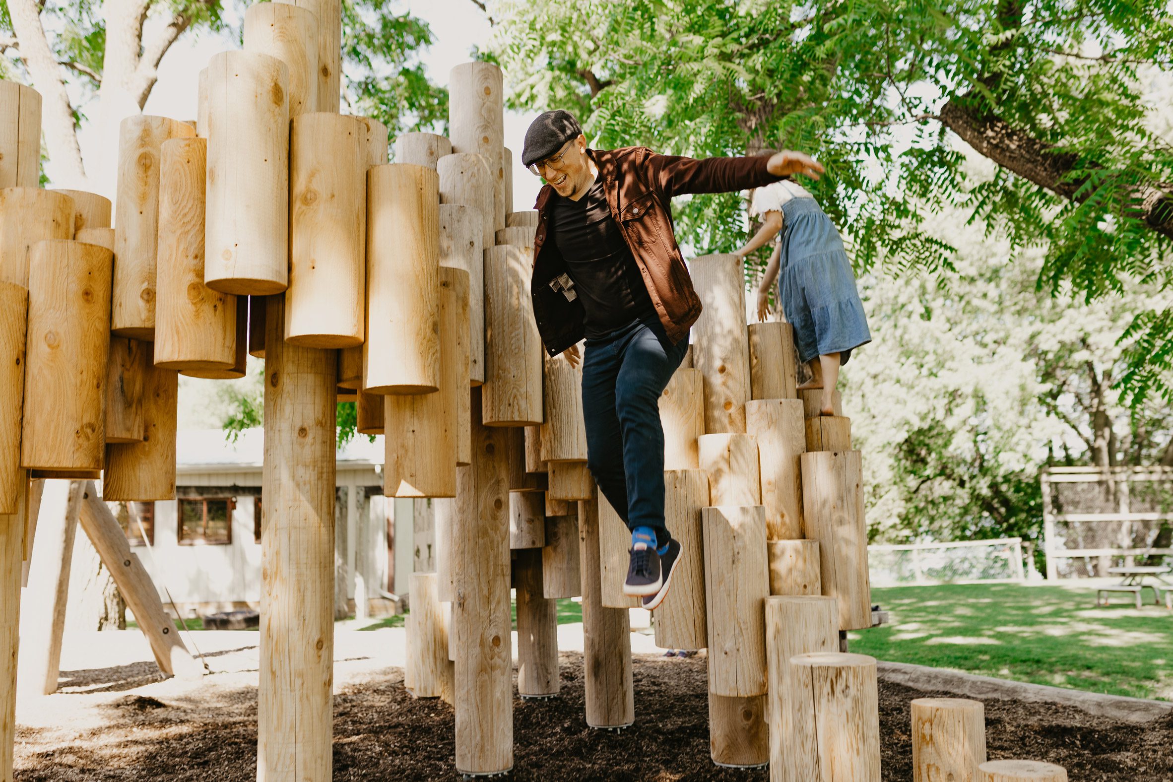 An adult leaping from leaping from a playground sculpture made of logs