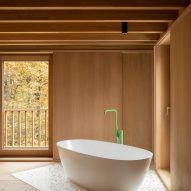 White freestanding bath with a green tap in a timber-clad room