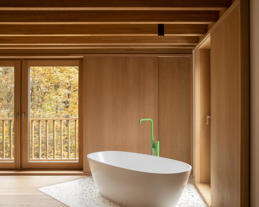 White freestanding bath with a green tap in a timber-clad room