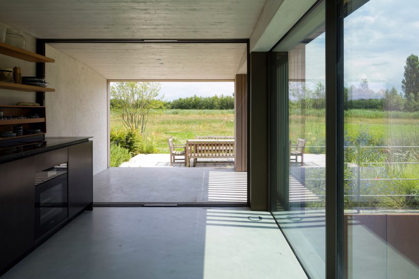 A boxy concrete kitchen with a wall opening leading to an outdoor garden