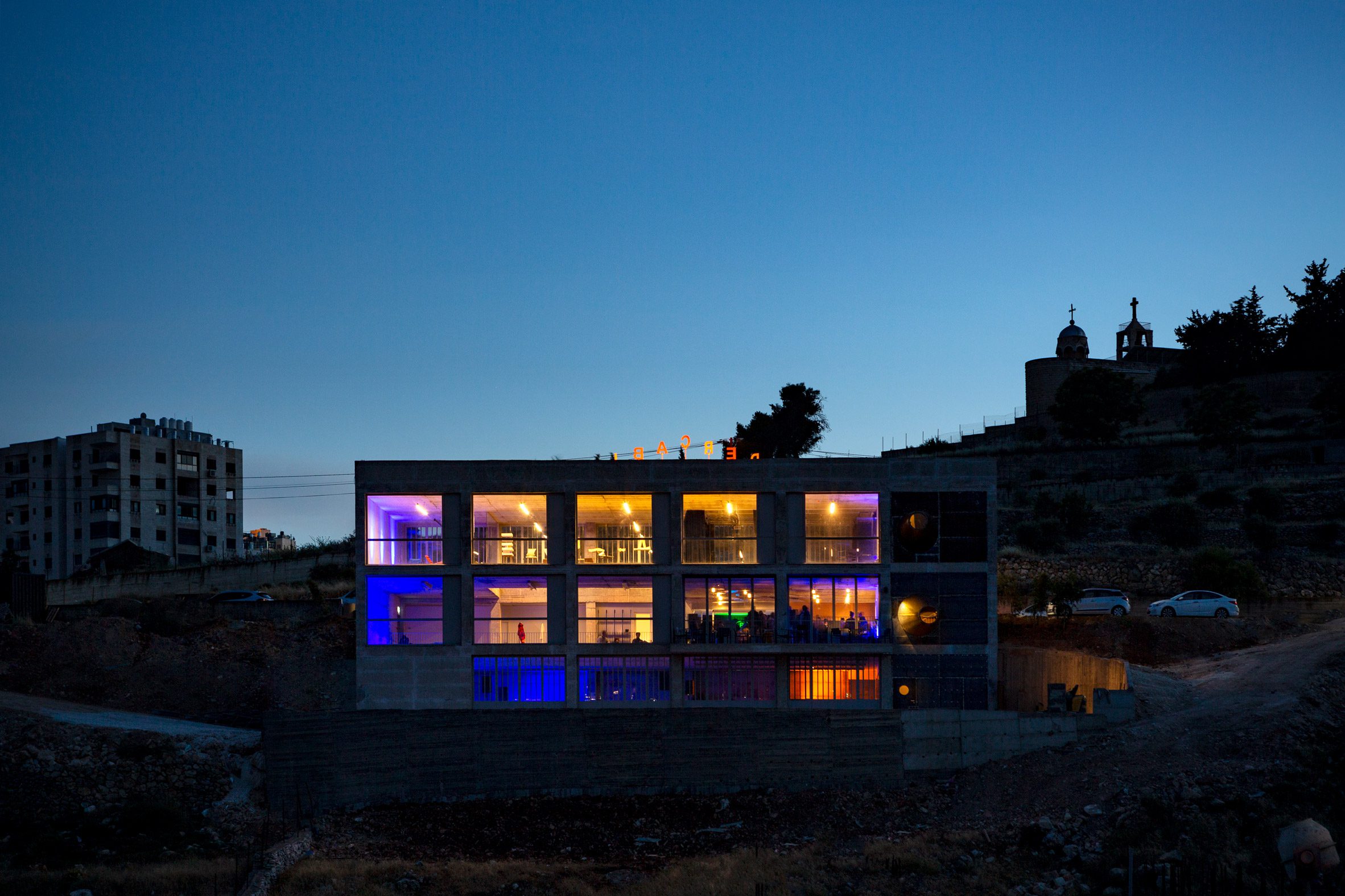 Photo of the Wonder Cabinet building with windows lit up in different colours at night from across the valley