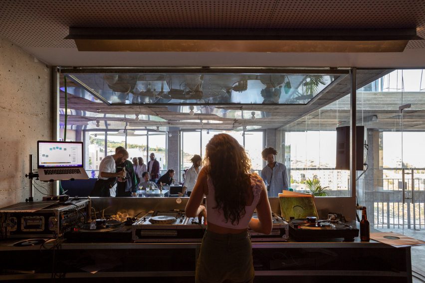 Фотография внутренней части диджейской будки с видом на пространство, похожее на кафе, где люди общаются с напитками.
