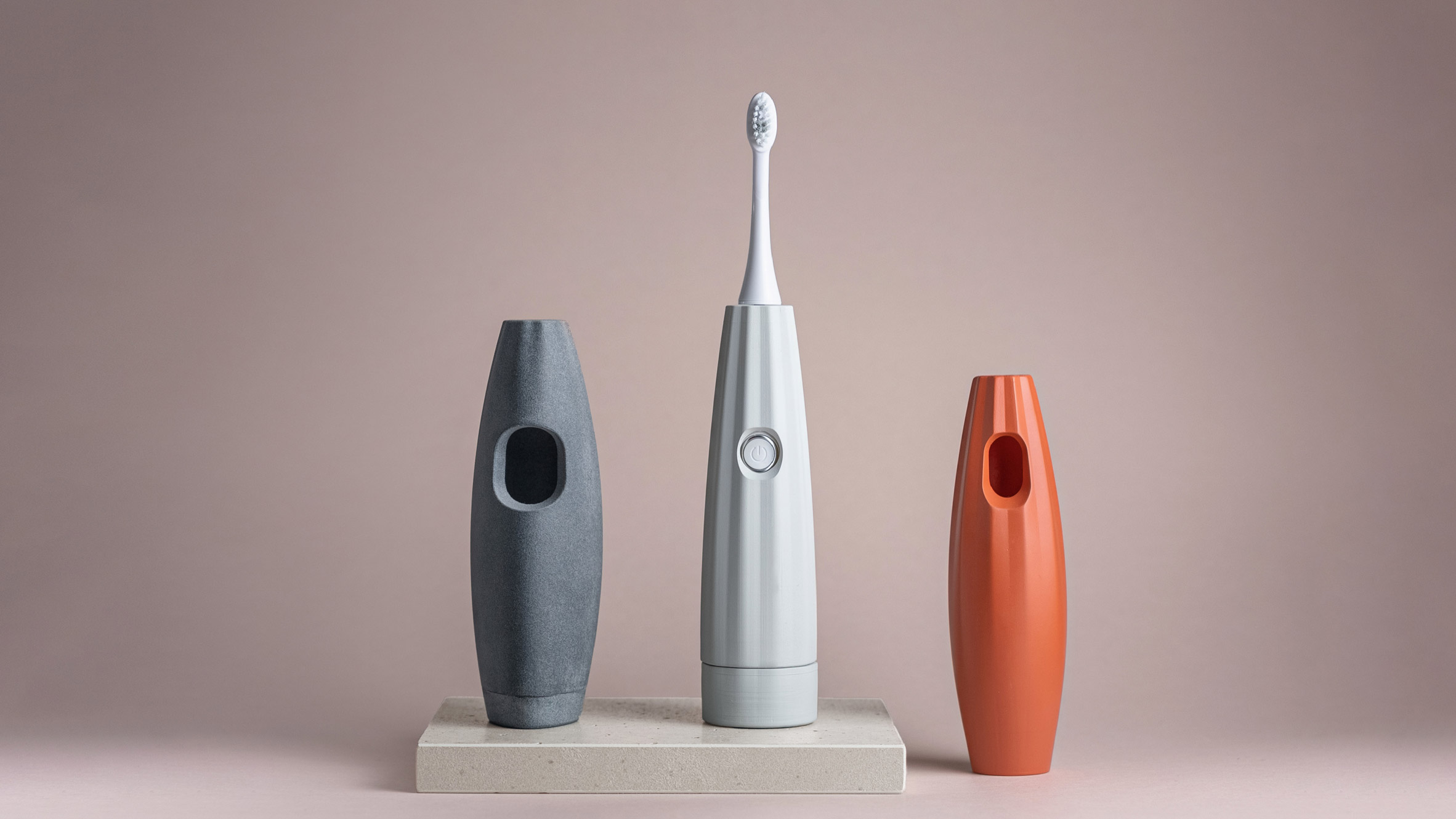 Photo of three of Landor & Fitch's 3D-printed toothbrush grips with a hole in the front to press the button on an electric toothbrush