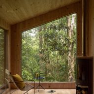 Interior of a timber cabin with large windows looking onto a forest