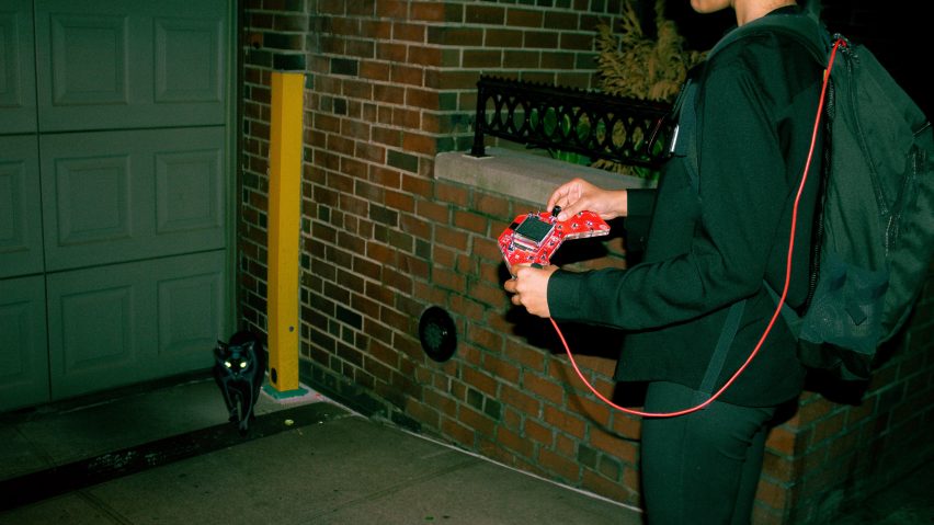 A person holding a red device with a cat in corner