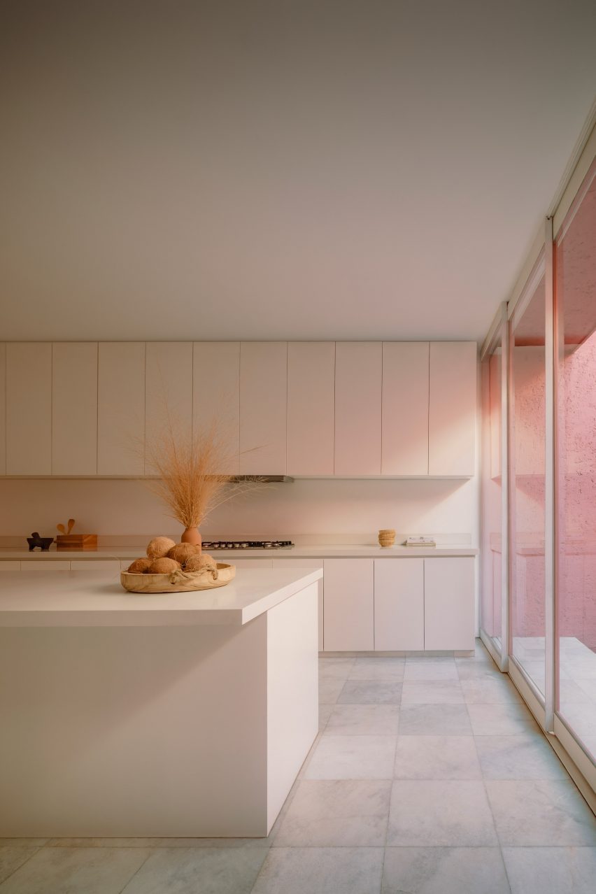 White kitchen with minimally detailed cabinets and pink light entering from the right