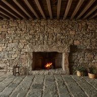 Room with stone walls and floors, timber ceiling beams and a fireplace