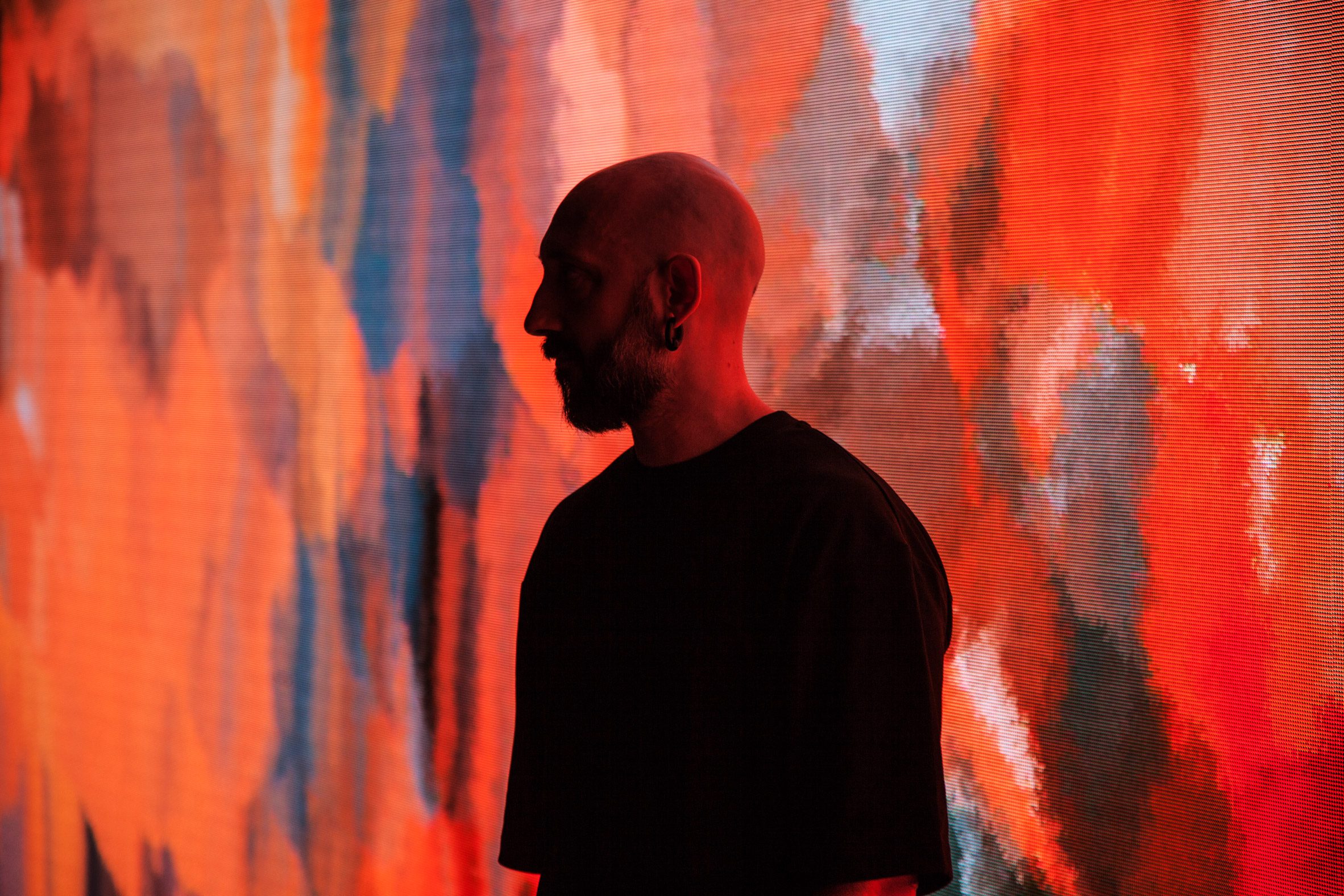 Headshot of the artist Quayola in shadow with his head held close to one of his artworks