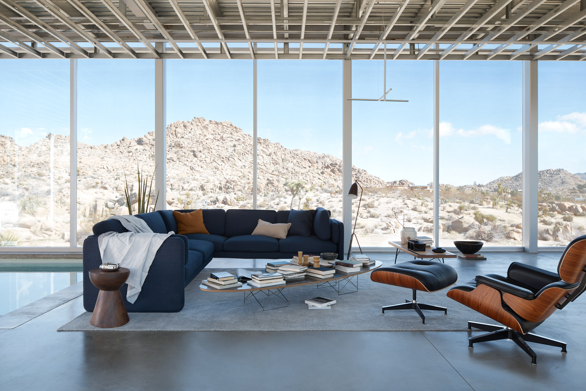 A blue sofa and a leather reclining chairs sit in front of a glazed wall looking over a desert