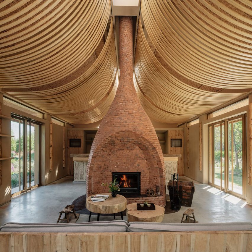 Strips of wood curve from the ceiling, while a central brick fireplace divides the open space