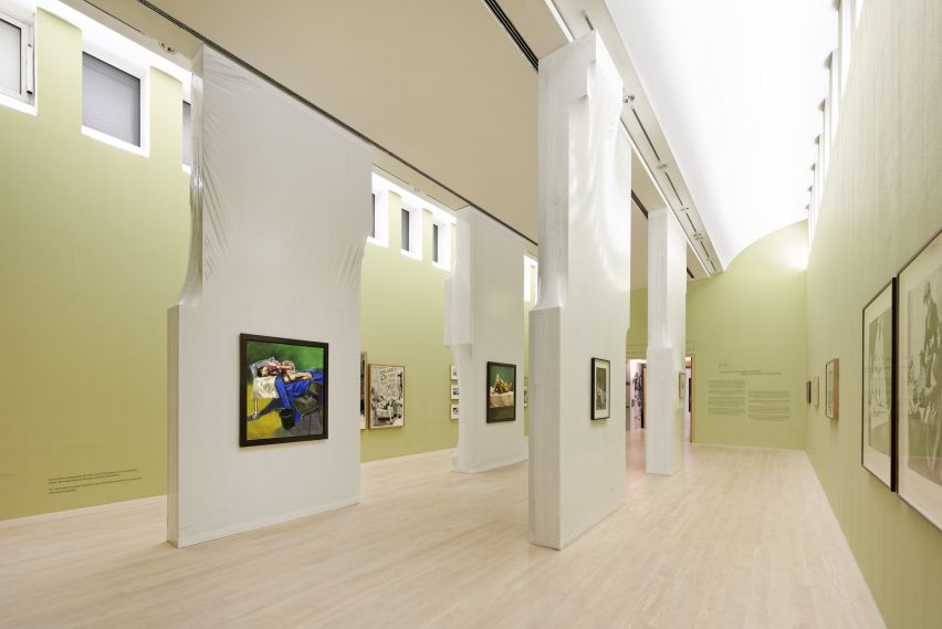 Pale green room with tall shrink-wrapped blocks displaying paintings
