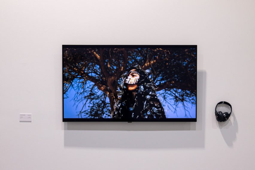 Photo of a screen mounted on a white wall showing a person in front of a tree