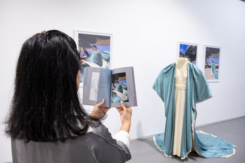 Photo of an exhibition with a blue and white garment on a mannequin and photographs of the garment being worn by a model
