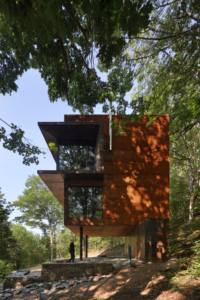Corten steel cabin on stilts with trees in foreground