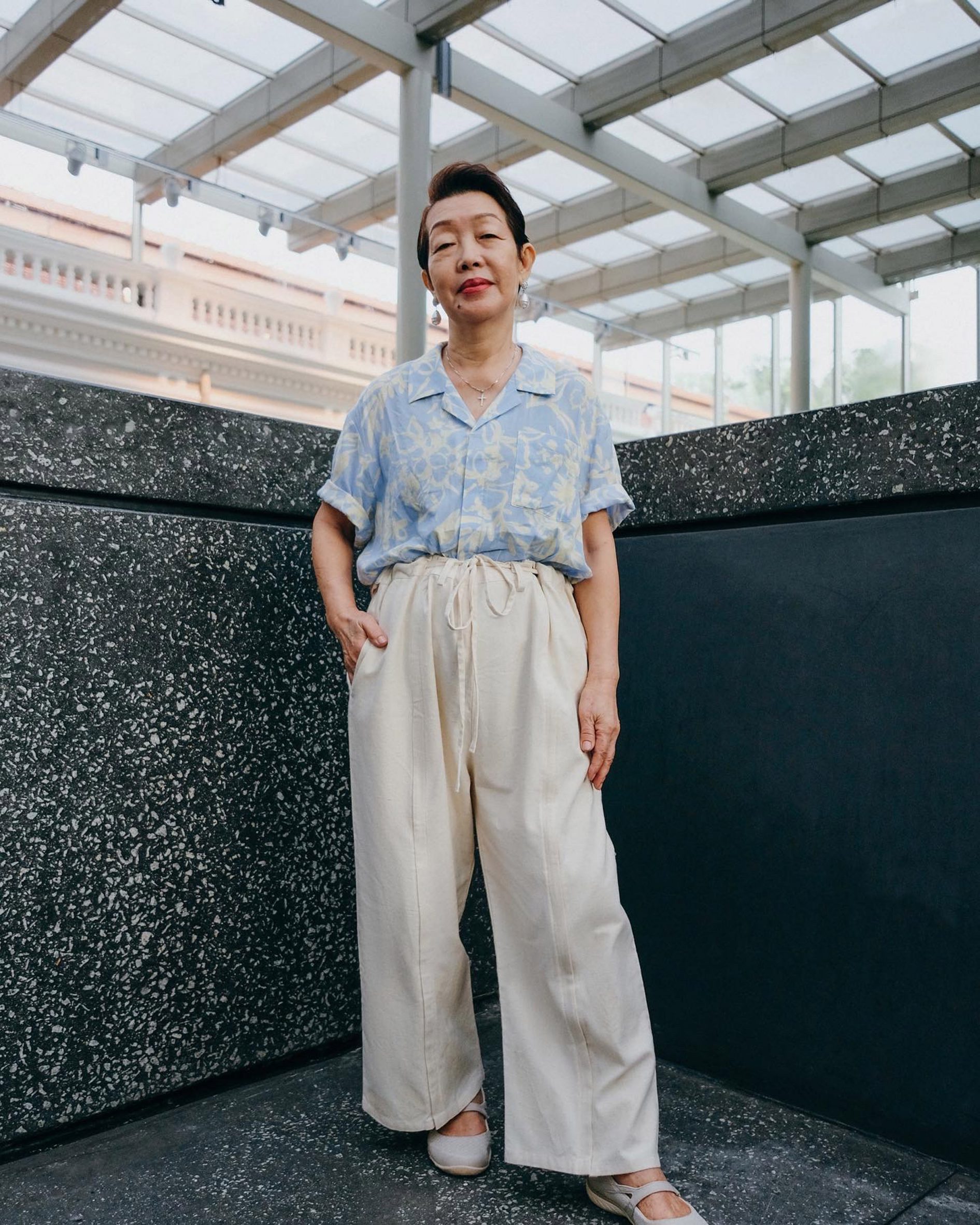 Photo of an elegant older model wearing a tropical-print light blue shirt and light beige trousers by Will & Well