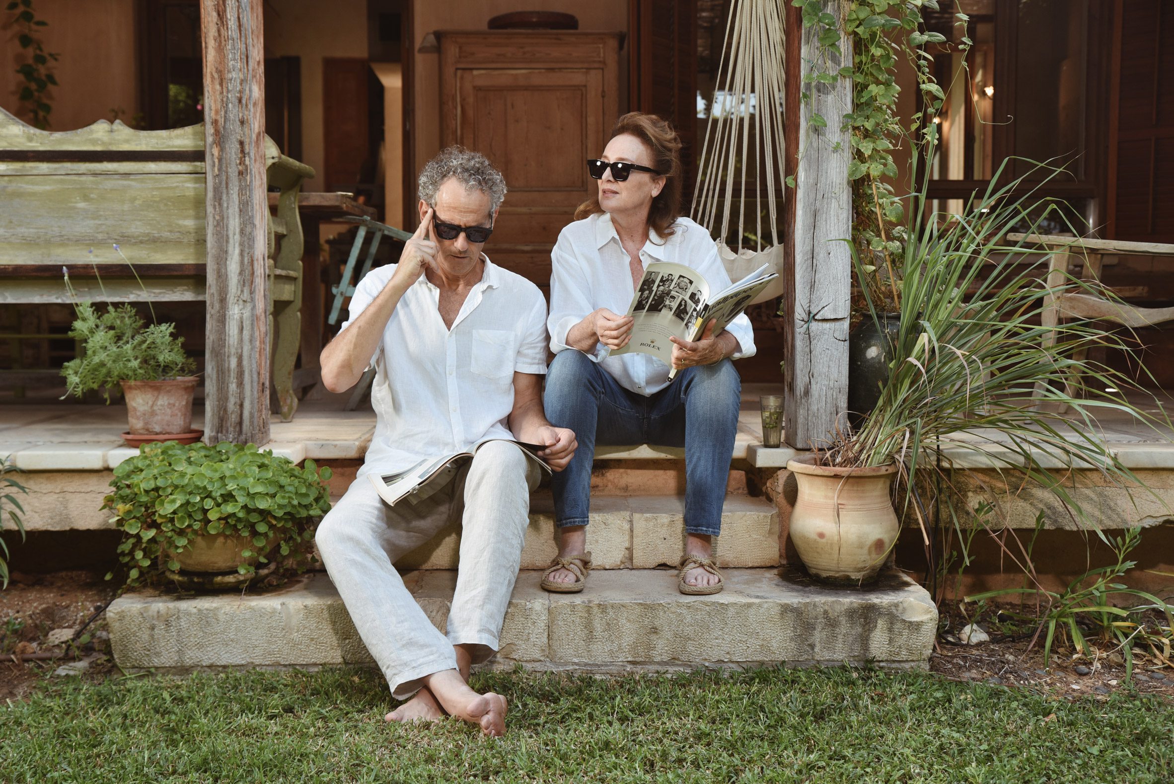 Photo of a middle-aged couple sitting on some garden steps wearing 32 North sunglasses. One of them is reading a magazine and the other is staring off into the distance