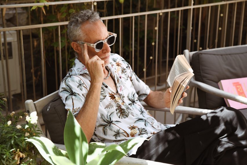 Photo of a silver-haired man in a Hawaiian shirt reading a paperback book on a garden chair outside