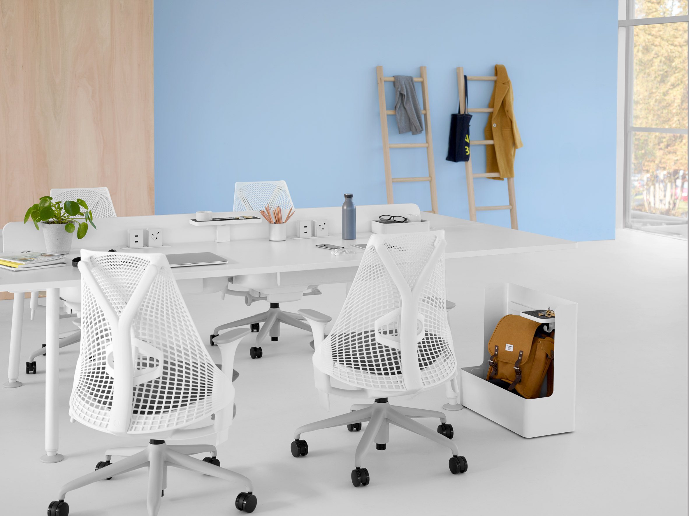 Herman Miller and Yves Béhar's Sayl chairs photographed around a shared work table in a clean and white office environment