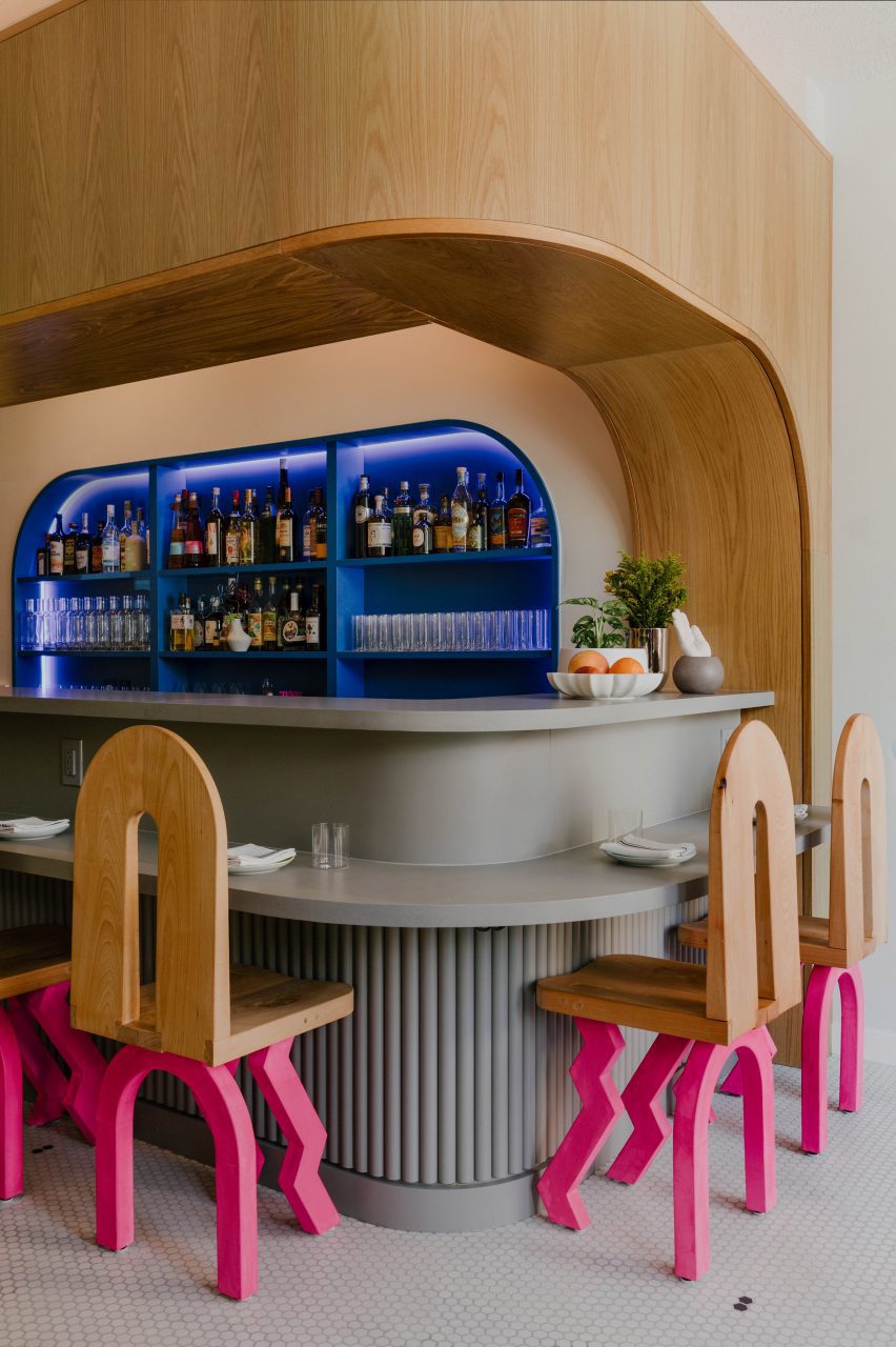 White oak arch over light grey bar counter, accompanied by hot pink chairs