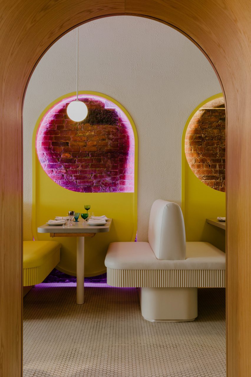 View through arch towards banquette seating and tables with exposed brick above