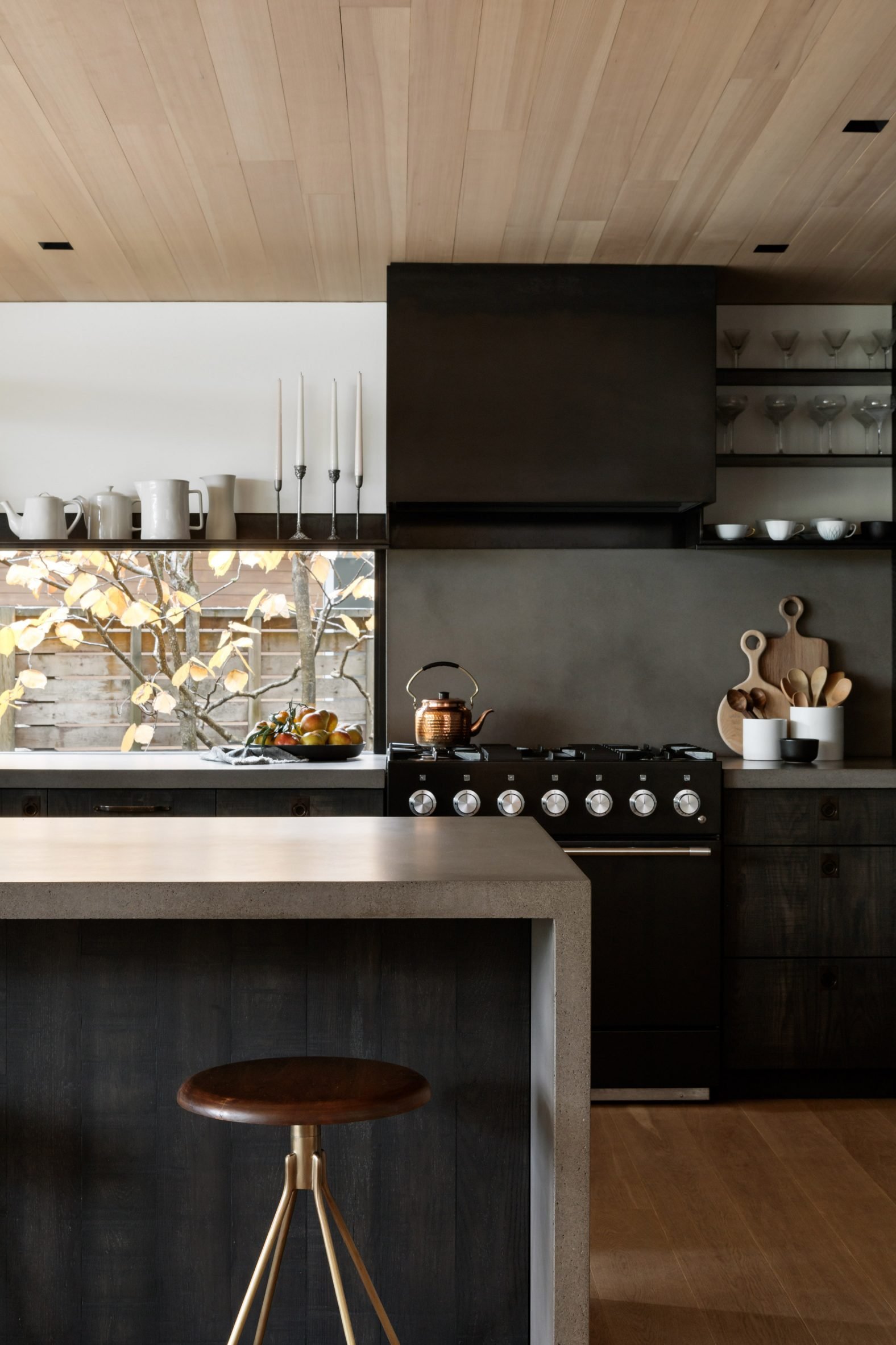 Dark-coloured kitchen with steel range hood and shelving
