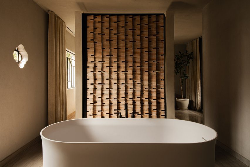 Freestanding bathtub in front of a partition of angled bricks