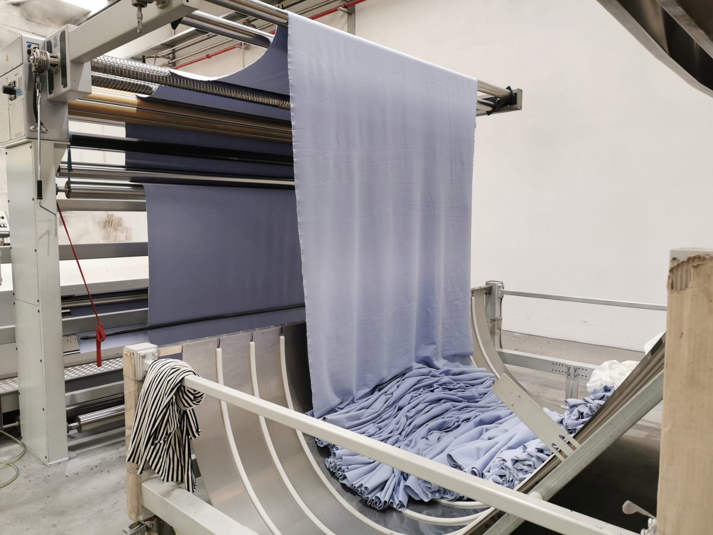 Photo of a pale blue fabric being pulled through industrial machines
