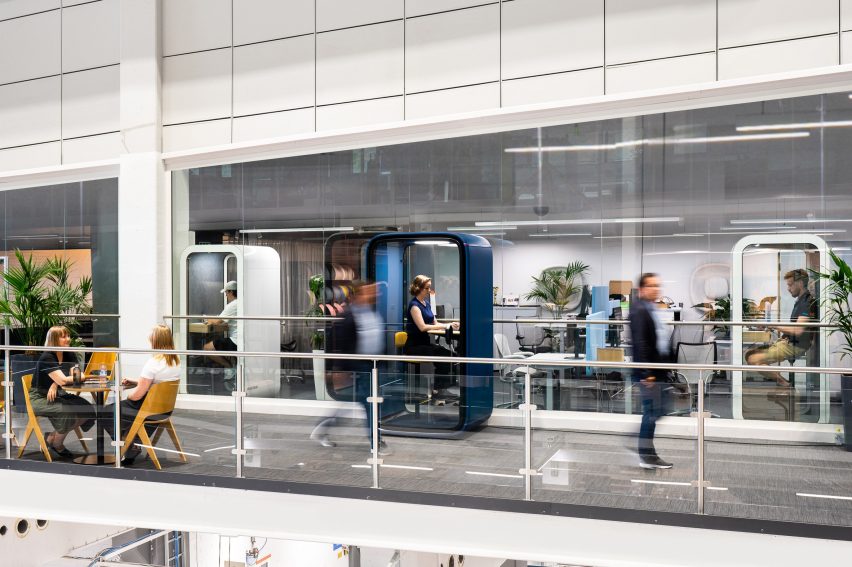 Photo or rendering of a modern, busy office incorporating several single-person work pods where people are working on their laptops in peace