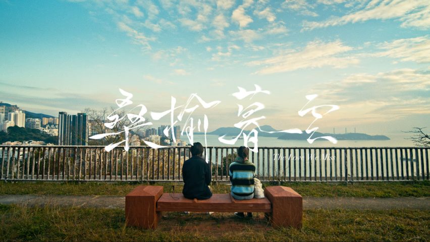 Frame from a film showing two figures sitting on a bench looking out over Hong Kong