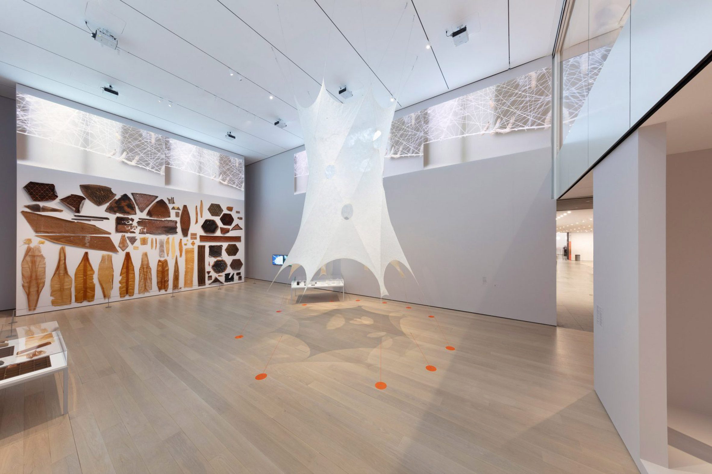 Photo of Neri Oxman's Silk Pavilion II – a tall, ethereal tube of sheer white silk material suspended between the floor and ceiling in the Museum of Modern Art New York
