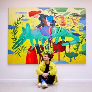 Jamie Hayon sitting in front of a painting featuring a person riding a green creature