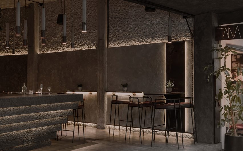 Cove-lit concrete walls with stools around small tables