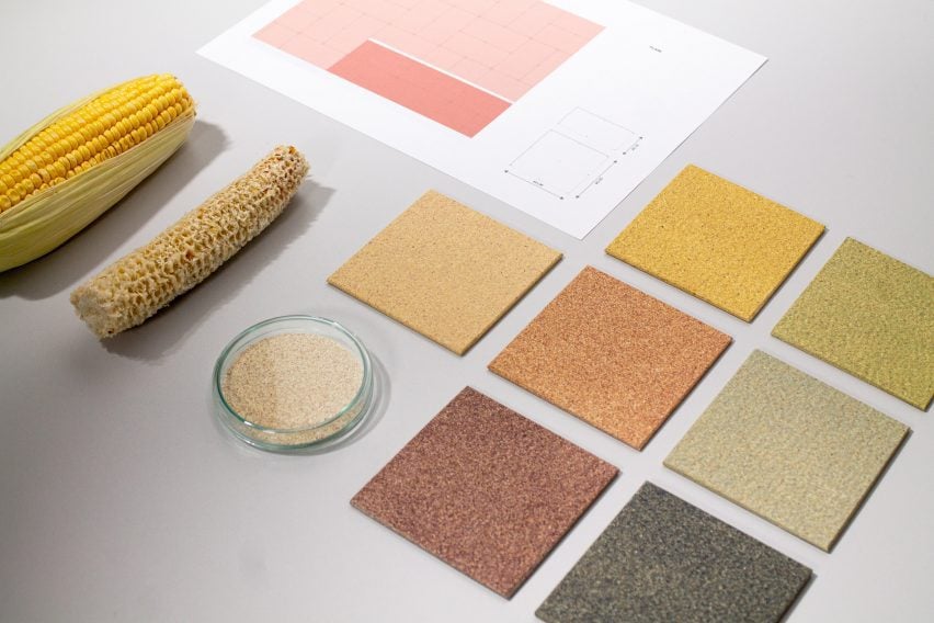 Photo of seven colours of CornWall tile in flatlay, ranging from a warm beige to a a muted reddish brown and a dark greenish grey. The tiles are arranged beside a bare corn cob, a full corn cob and a small bowl of shredded biomass