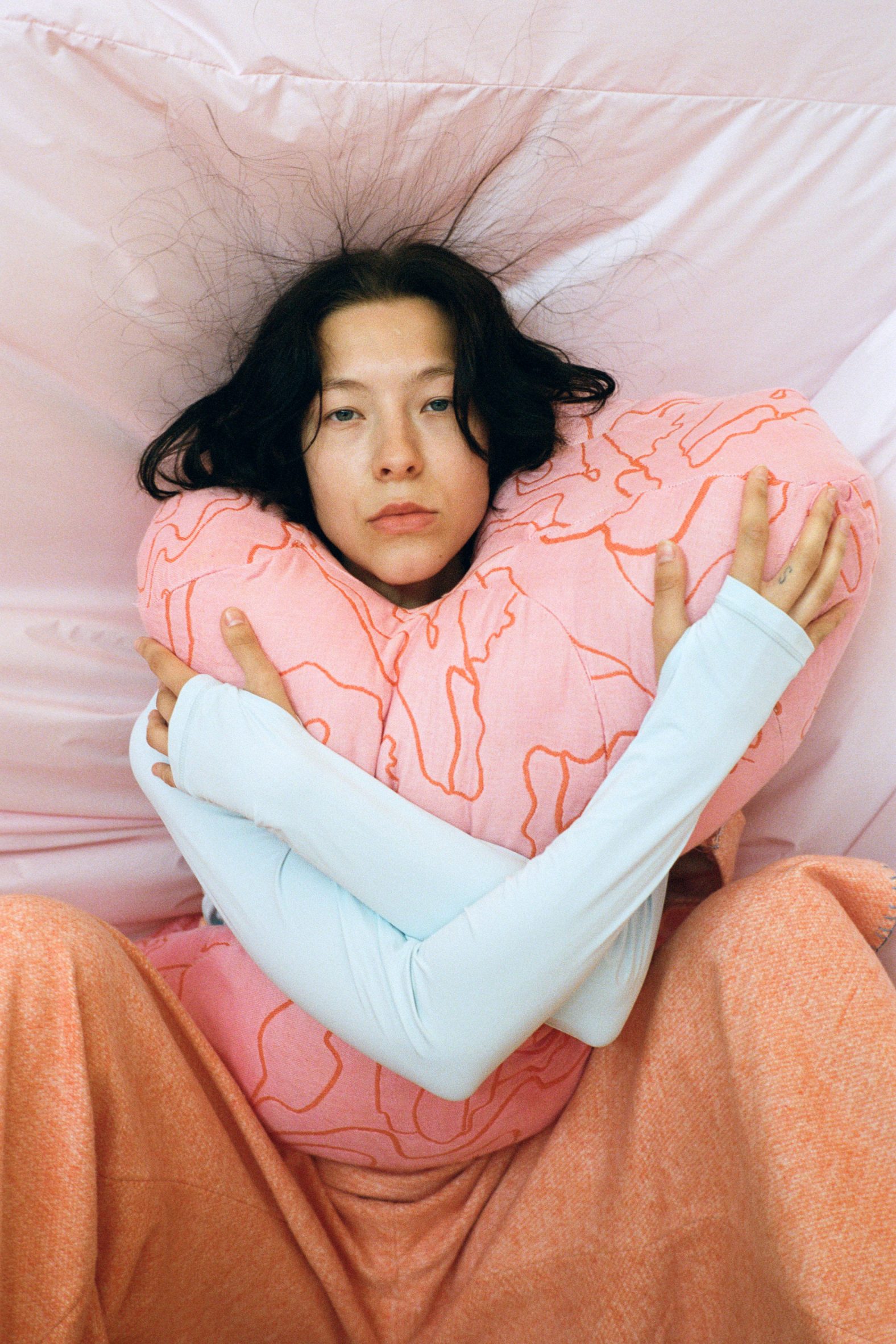 Seated model clutching a soft pink wearable sculpture