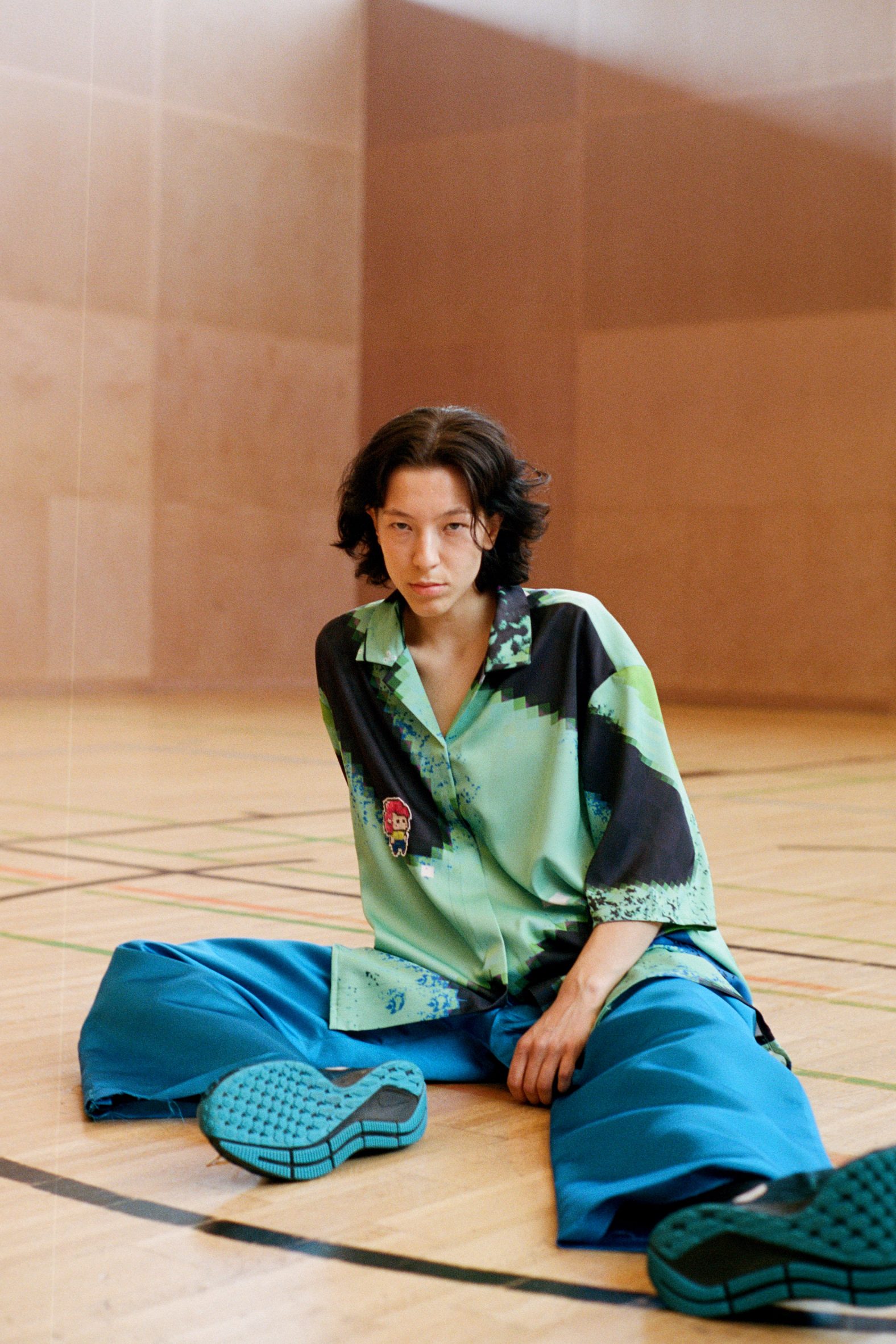 Seated model wears blue trousers and green and black shirt