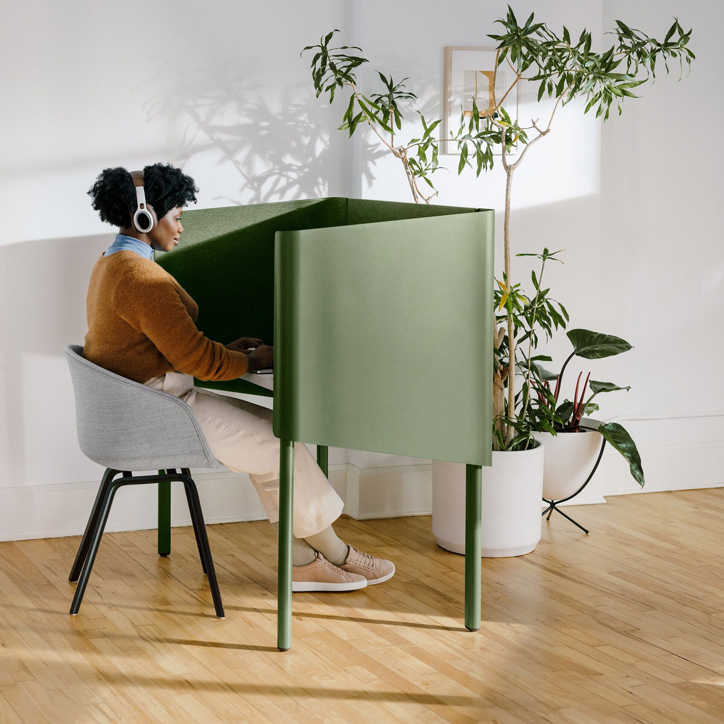 Woman sits at green enclosed desk 