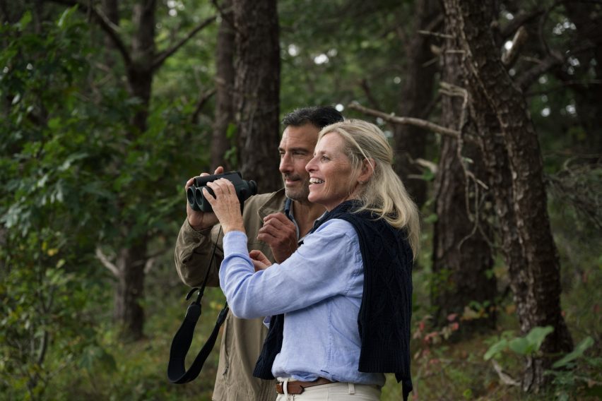 Photo of a man and a woman in nature sharing a pair of binoculars between them