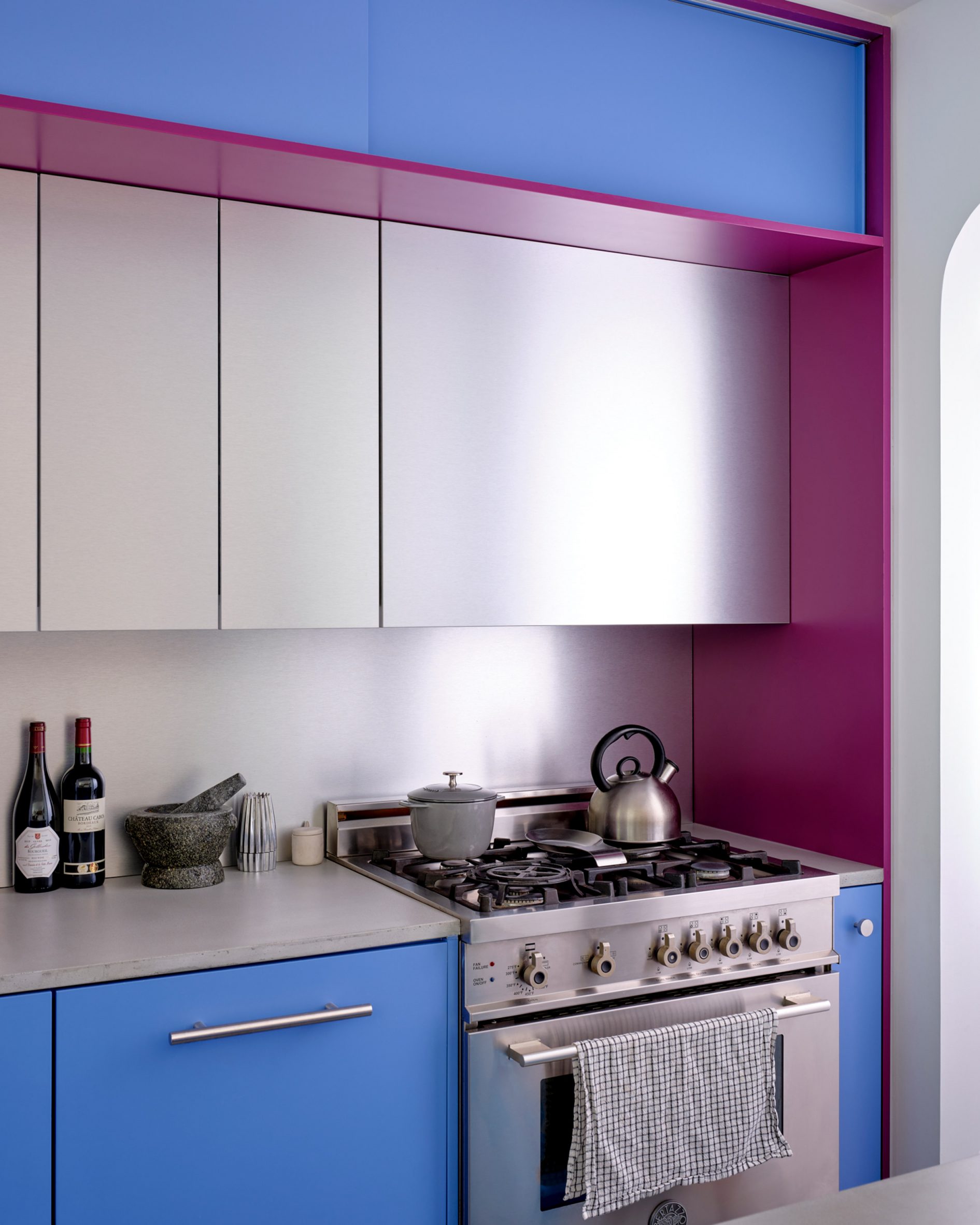 Raspberry and periwinkle cabinets surrounding a cooking area, which also features aluminium panels