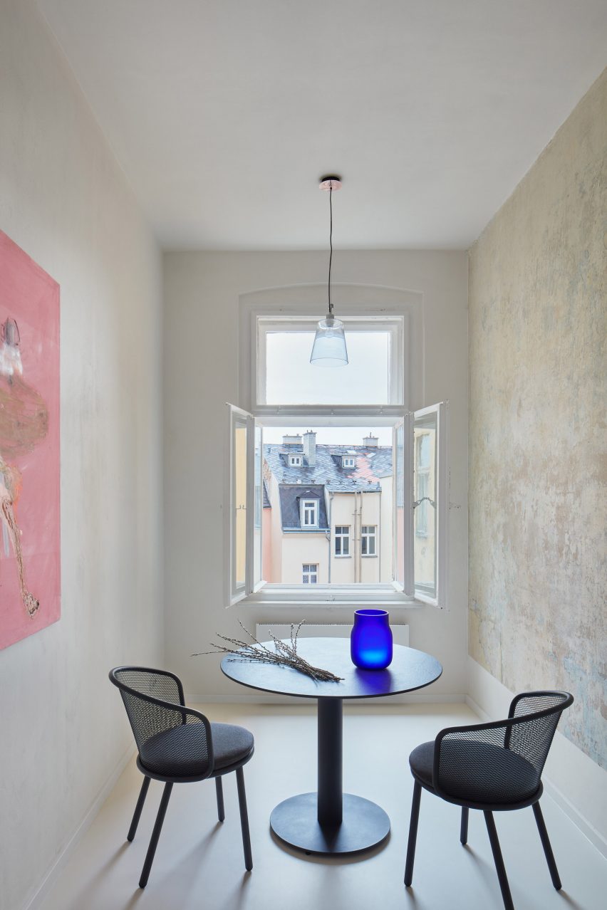 Round dining table and chairs in front of open window in narrow room